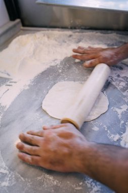 Aşçı ya da aşçı elleri hamurun üzerine mermer masa, fırın arka planı, üst görünüm, pizza, turta ya da ekmek hamuru serpiştirmeye devam ediyor.