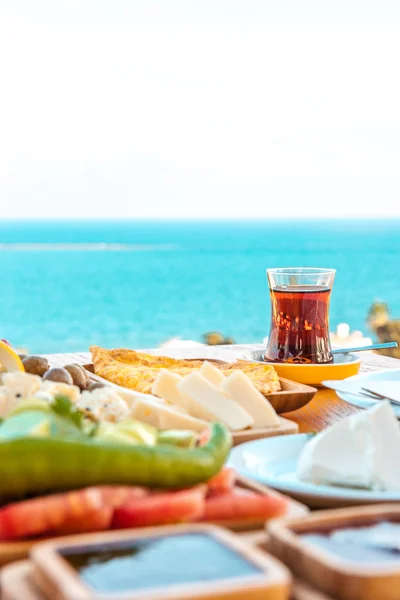 Turkish tea with breakfast on the table in front of sea background landscape at Summer season. Turkish or Greek Breakfast at seaside. Breakfast on the beach at hotel or resort by the sea in summer season. Holiday and vacation breakfast image.