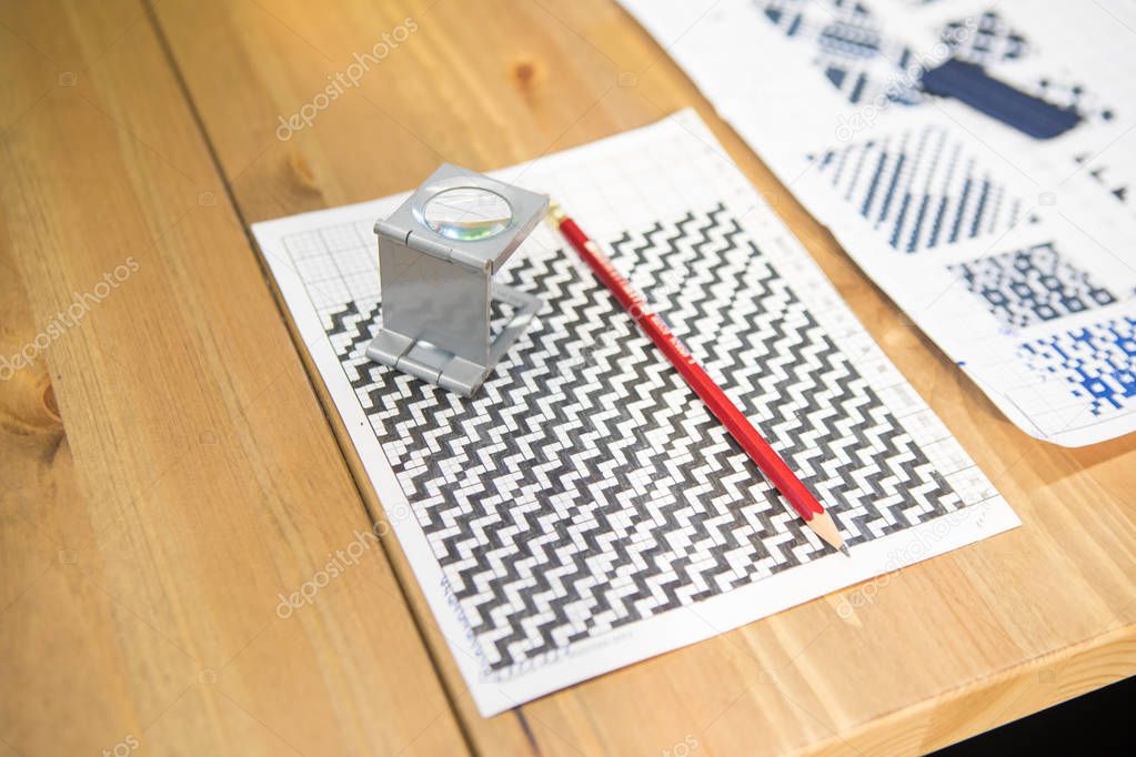 Textile fabric pattern sketch on the paper, magnifier and pencil. Textile industry concept background image.