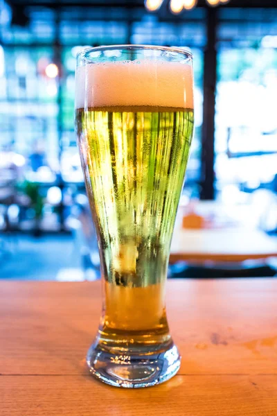 Glass of beer on old wooden table in cafe, restaurant or bar. Nightlife concept image. Cold Beer glass on the wooden desk in the retro vintage bar interior. This beer is draught and lager.