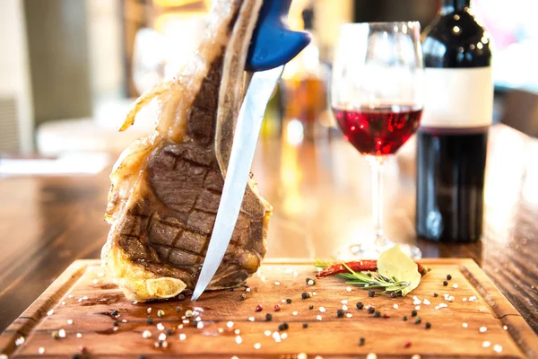Romantic Dinner with wine in the restaurant. Grilled tasty delicious vertical lamb chop and glass of wine and bottle on wooden board and rustic wood table with knife and herb