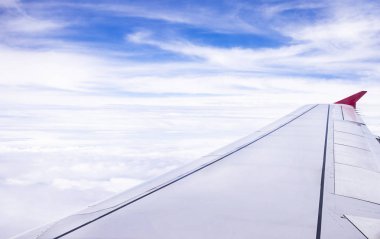 Uçan bir uçağın kanadı Beyaz bulutlarla mavi arka planda