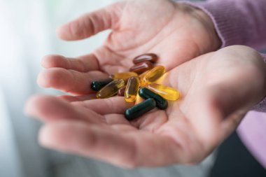 Omega 3 ve diğer vitamin bileşiklerinden oluşan kapsüller taşıyan orta yaşlı beyaz bir kadının ellerini yakın plan çekiyoruz.
