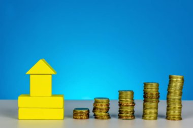 Gelecek için yatırım. Tasarruf ve yatırım için rüya evi ve zaman kavramı kaydetmek için. Ev ahşap küp ve sikke üzerinde mavi arka plan istifleme.