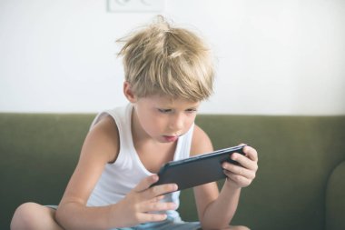 Çocuk sarı saçlar tablet yatak döşeme oyun oynamayı. ev iç. modern cihaz teknolojileri seçici odak