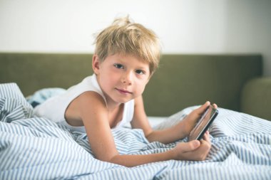 Çocuk sarı saçlar tablet yatak döşeme oyun oynamayı. ev iç. modern cihaz teknolojileri seçici odak