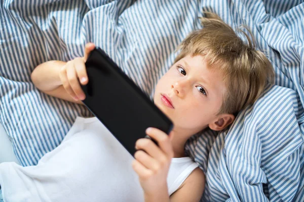 Çocuk sarı saçlar tablet yatak döşeme oyun oynamayı. ev iç. modern cihaz teknolojileri