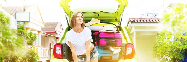 Uzun banner. Kadının yanına yeşil araba şeyler ile aşırı yüklü. Seyahat hazır. Parlak bavul bagaj aksesuarlar giysileri. Yaz kavramı tatil macera