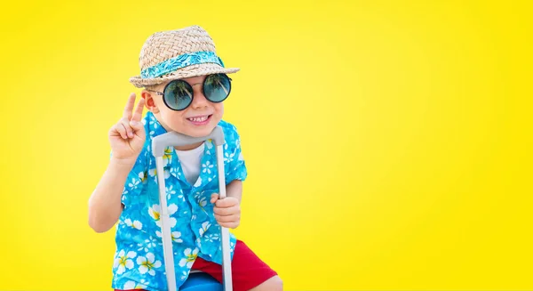 幸せなダンディ少年ハワイアン シャツ麦わら帽子準備ができて座っているスーツケース旅行夢自由旅行概念分離された黄色の背景に — ストック写真