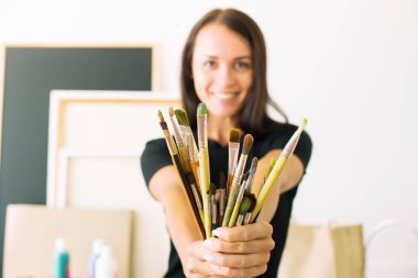 Mutlu genç ressamın kız siyah elbise petrol ve suluboya çizimi için Grup fırçalar elinde tutan sanatçının kavramı bulanık arka plan seçici odak nesne üzerinde