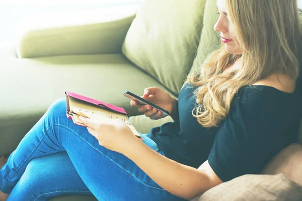 Businesswoman in jeans working at home office with smartphone and daily log Rest on green soft sofa Lifestyle Copy space Toned