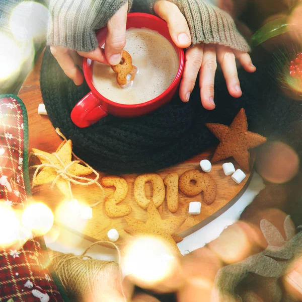 Female hand holds 8 from expiring year to celebrate 2019 fresh hot cup beverage coffee with gingerbread cookies Magic bokeh Dark background Top view Flat lay Winter cozy theme