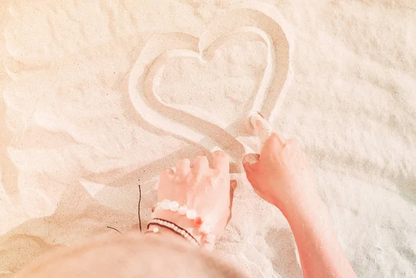 Female hands drawing heart on sand closeup