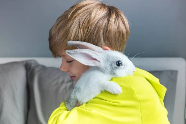 Niño feliz en chaqueta amarilla jugando conejo — Foto de Stock