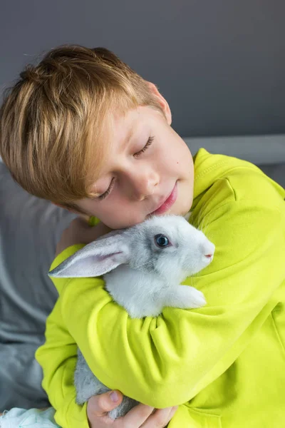 Niño feliz en chaqueta amarilla jugando conejo — Foto de Stock