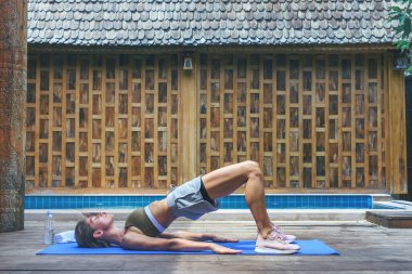 Köprü pozisyonu. Genç, formda bir kadın, ahşap arka planda yüzme havuzunun yanında yoga germe egzersizi yapıyor. Kadın havuz güvertesinde meditasyon yapıyor..