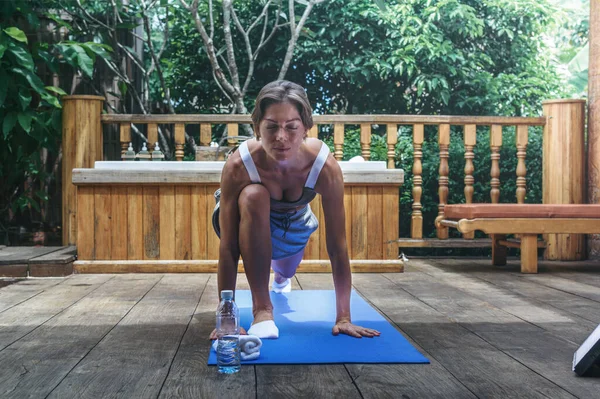 Hilal hareketi pozu veren bir kadın. Genç, formda bir kadın, ahşap arka planda, yüzme havuzunun yanında yoga esneme egzersizi yapıyor. Kadın havuz güvertesinde meditasyon yapıyor..