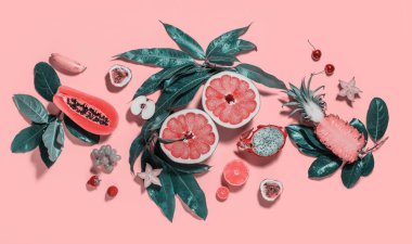 Farklı egzotik tropikal meyveler ve parlak pembe arka planda yeşil yapraklarla iki yarıya bölünmüş greyfurt. Çiğ yemek yeme konsepti. Süper doğal yiyecek.