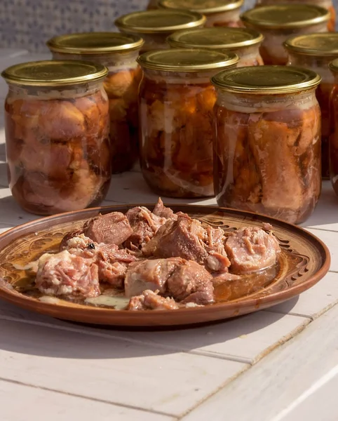 Canned meat in a glass jar on a white wooden table. Next plate with meat