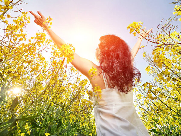 woman in white dress standing back with raised hands in yellow flowers field