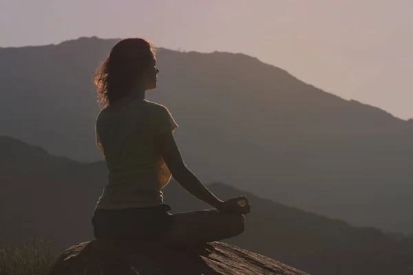 Kvinnan sitter på berget och mediterar i yogaställning. Bakifrån — Stockfoto