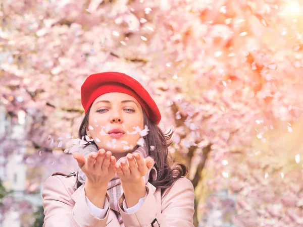 Schöne Frau bläst Blütenblätter und genießt einen blühenden Frühlingsgarten — Stockfoto