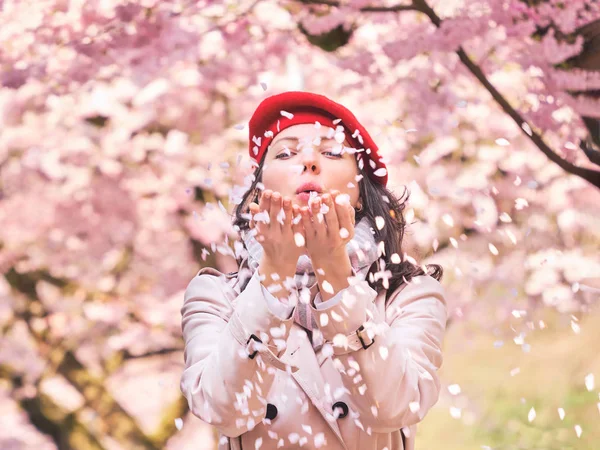 Piękna kobieta dmuchanie płatków w jej rękach, ciesząc się kwitnący ogród wiosenny — Zdjęcie stockowe