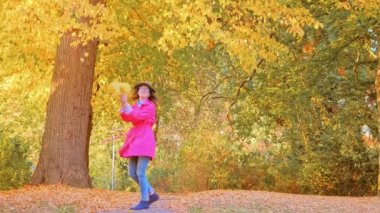 Parkta sonbahar yapraklarıyla oynayan mutlu kadın.