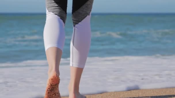 Çıplak ayaklı kadın sahilde yürüyor, deniz dalgaları ayaklarını yıkıyor. — Stok video