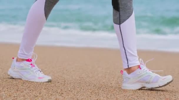 Okyanus sahilinde yürüyen genç kadın, kamera ayakların üzerinde hareket ediyor. — Stok video