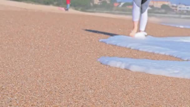 Holohlavá žena kráčející po pláži, mořské vlny mu myjí nohy, oceánské pobřeží — Stock video