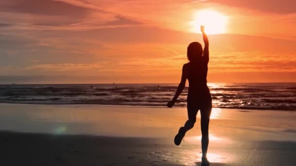 Тонкая женщина в спортивной одежде с поднятыми руками на берегу океана — стоковое видео