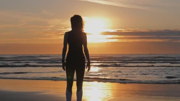 Silueta de mujer delgada con los brazos levantados en la playa al atardecer — Vídeo de stock