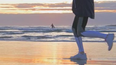 Gün batımında sahilde koşan kadın, ıslak kum ayak izleri.