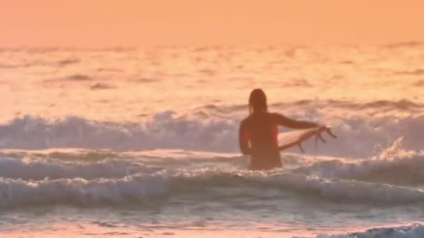 Surfařka se svým surfařem kráčí k vlnám oceánu při západu slunce — Stock video