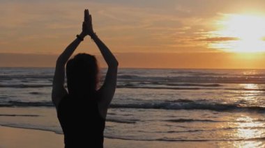 Kumsalda kolları havada bir kadın yoga nefesli teknikler üzerinde çalışıyor.