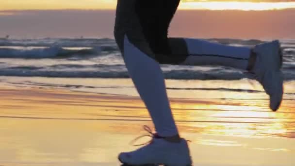 Una mujer corriendo por la playa al atardecer. Calzado deportivo, huellas de arena mojada — Vídeo de stock