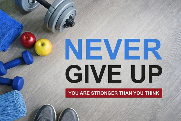 Never Give Up. You Are Stronger Than You Think. Fitness motivational quotes.Sport theme. Healthy and active lifestyle concept. Sneakers, dumbbells, apples and a workout mat on grey wooden background.