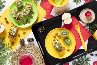 Sağlıklı gıda. Üstten görünüm dekorasyon tatil arka plan. Düz yatıyordu. Waffle, kivi, badem, yumuşak peynir, elma, modern kırmızı ve beyaz peçeteler, beyaz arka plan üzerinde süt ile kahvaltı.