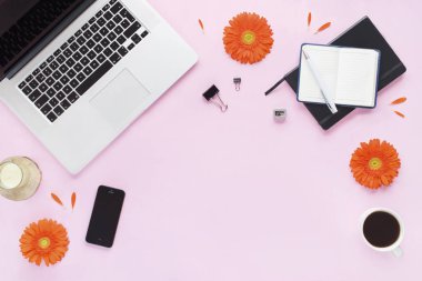 Ev ofis büro. Dizüstü bilgisayar, telefon, kalem, mum, kahve kupa, portakal çiçekleri ve yaprakları pembe bir arka plan üzerinde siyah günlüğü ile kadın çalışma alanı. Düz yatıyordu, en iyi görünüm. Moda blog bakmak. Metninizi ekleyin.