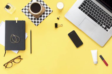 Ev ofis büro. Dizüstü bilgisayar, telefon, kalem, mum, Bayan Kozmetik aksesuarlar, kahve kupa, sarı zemin üzerine siyah günlüğü ile kadın çalışma alanı. Düz yatıyordu, en iyi görünüm. Moda blog bakmak. Metninizi ekleyin.