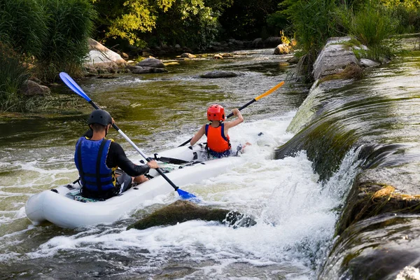 Parlak loitering sporcularda ve Koruyucu baretler bir şişme botla kürek kürek ile iki çocuk akıntıyla birlikte mücadele yarışmalar fırtınalı bir nehirde rafting katılan