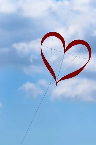 Red kite in the shape of heart in the blue sky with clouds at the festival of kites symbolizes love happiness in the wedding of a happy life