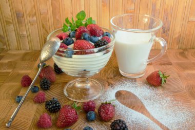 Bir fincan süt ve varlıklı bir yanındaki masada cam vazoda süt tatlı çilek ahududu ahududu blueberry yaban mersini ve nane yaprakları