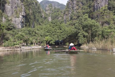 Ninh Binh, Vietnam - 30 Aralık 2016: Tam Coc kısmında Ninh Binh Eyaleti, Vietnam STK Dong Nehri boyunca tekne seyahat turistler. Kürekleri itmek için ayaklarını kullanarak kürekçi. 