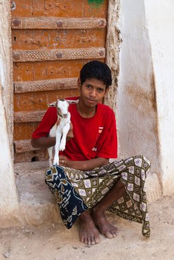 Eski bir ahşap kapı önünde oturan bir çocuk onun kollarında genç bir keçi 8 Mayıs, 2007 Şibam, Yemen tutar