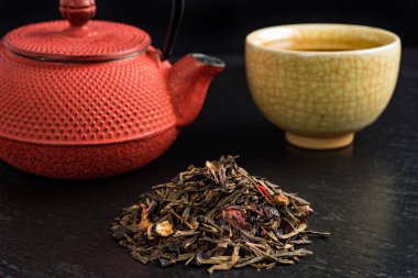 Fincan çay ve Japon geleneksel tarzı kırmızı çaydanlık ön planda kuru çay ile siyah çanak üzerinde