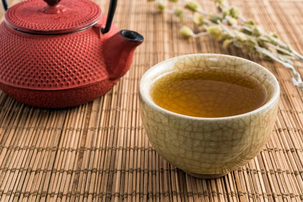 Cup of tea and japanese traditional style red teapot with dry tea on natural matting