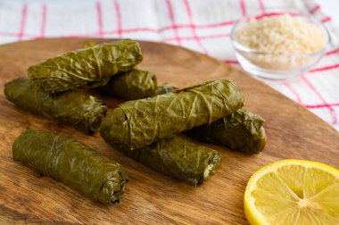 Lezzetli dolma yaprak (Akdeniz mutfağının geleneksel dolma) ahşap kesme tahtası limon dilimi ve küçük cam kase çiğ pirinç üzerinde