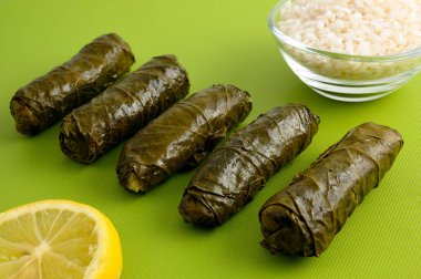 (Akdeniz mutfağının geleneksel dolma) yeşil kesme tahtası üzerinde limon dilimi ve küçük cam kase çiğ pirinç lezzetli dolma üzüm yaprakları